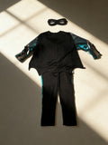 Boys dark hero jumpsuit costume set with cape and eye mask. Simulated muscle print and bat emblem design. Ideal for Halloween, themed parties, school dress-up and kids superhero role-play activities.